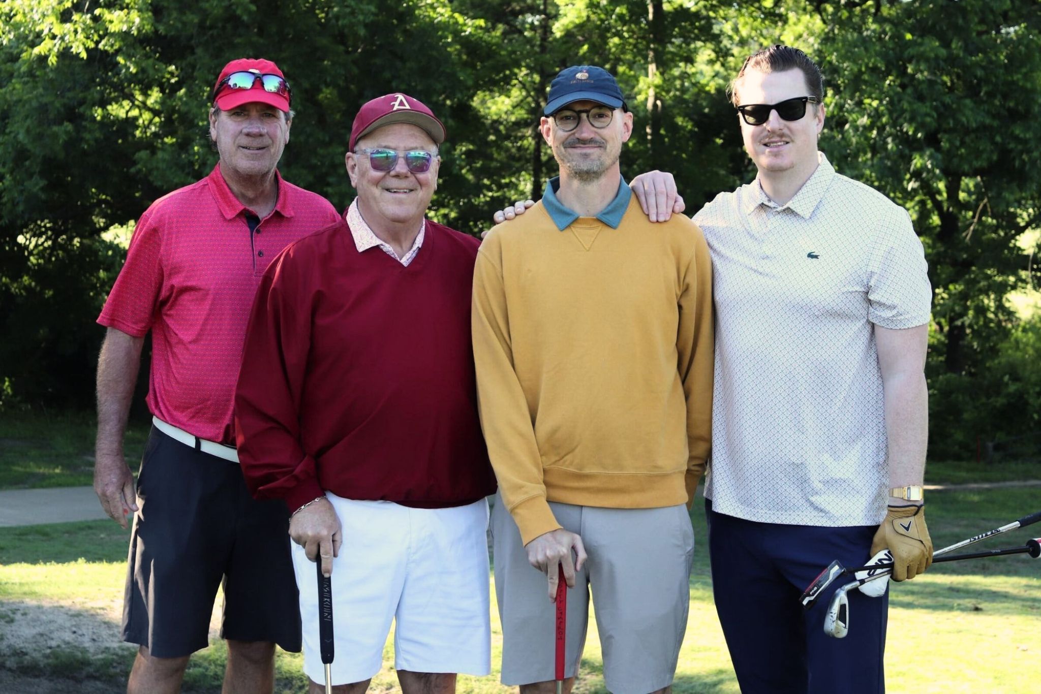 four men smiling holding golf clubs