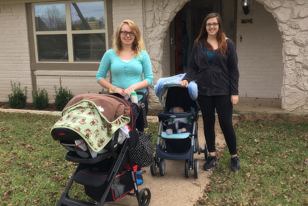women smiling and standing next to baby carriages outside of a house
