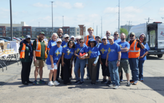 large group of volunteers from different organizations stand together smiling after distributing food
