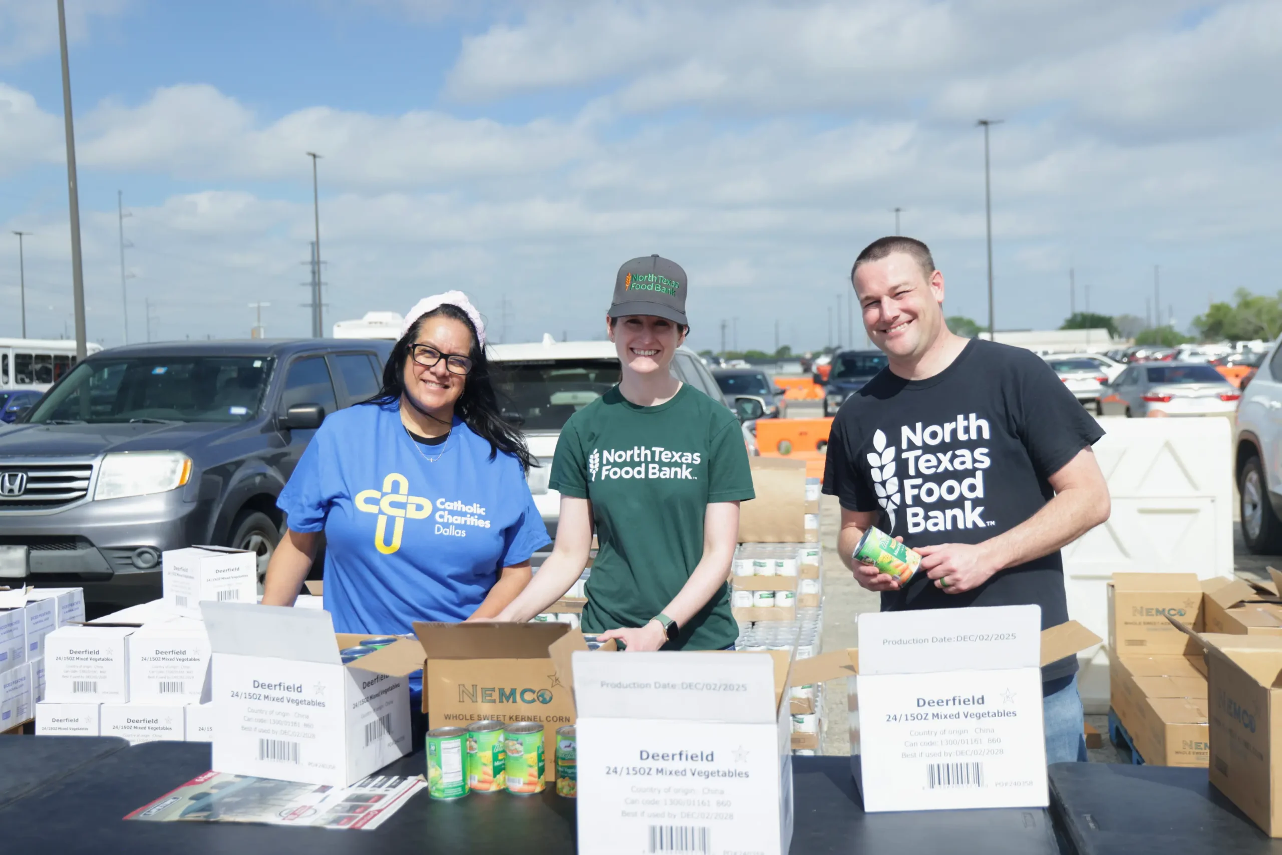 three volunteers, two from north texas food bank, and one from catholic charities dallas, standing together smiling while distributing food