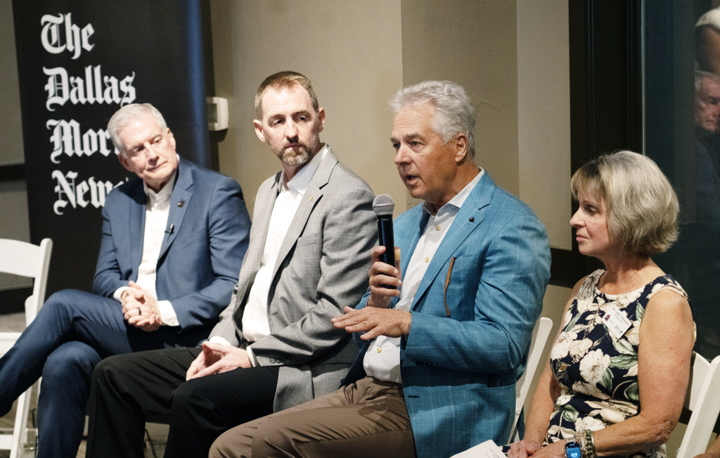 Catholic Charities Dallas CEO Dave Woodyard speaks into a microphone during a panel discussion on the future of Collin County, seated alongside local government, business, and nonprofit leaders.